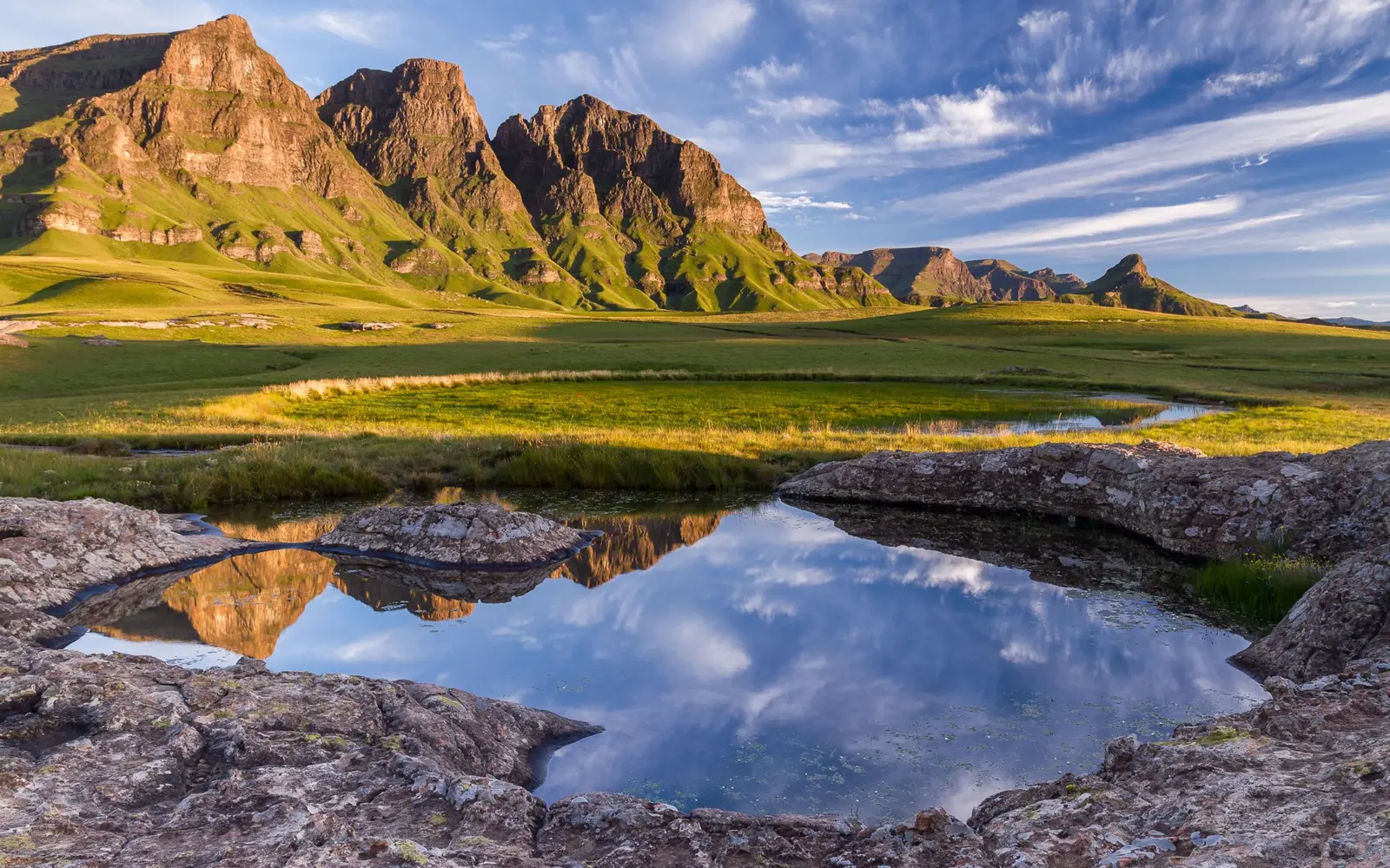 Green highland peaks reflected in a mountain pool in Lesotho
